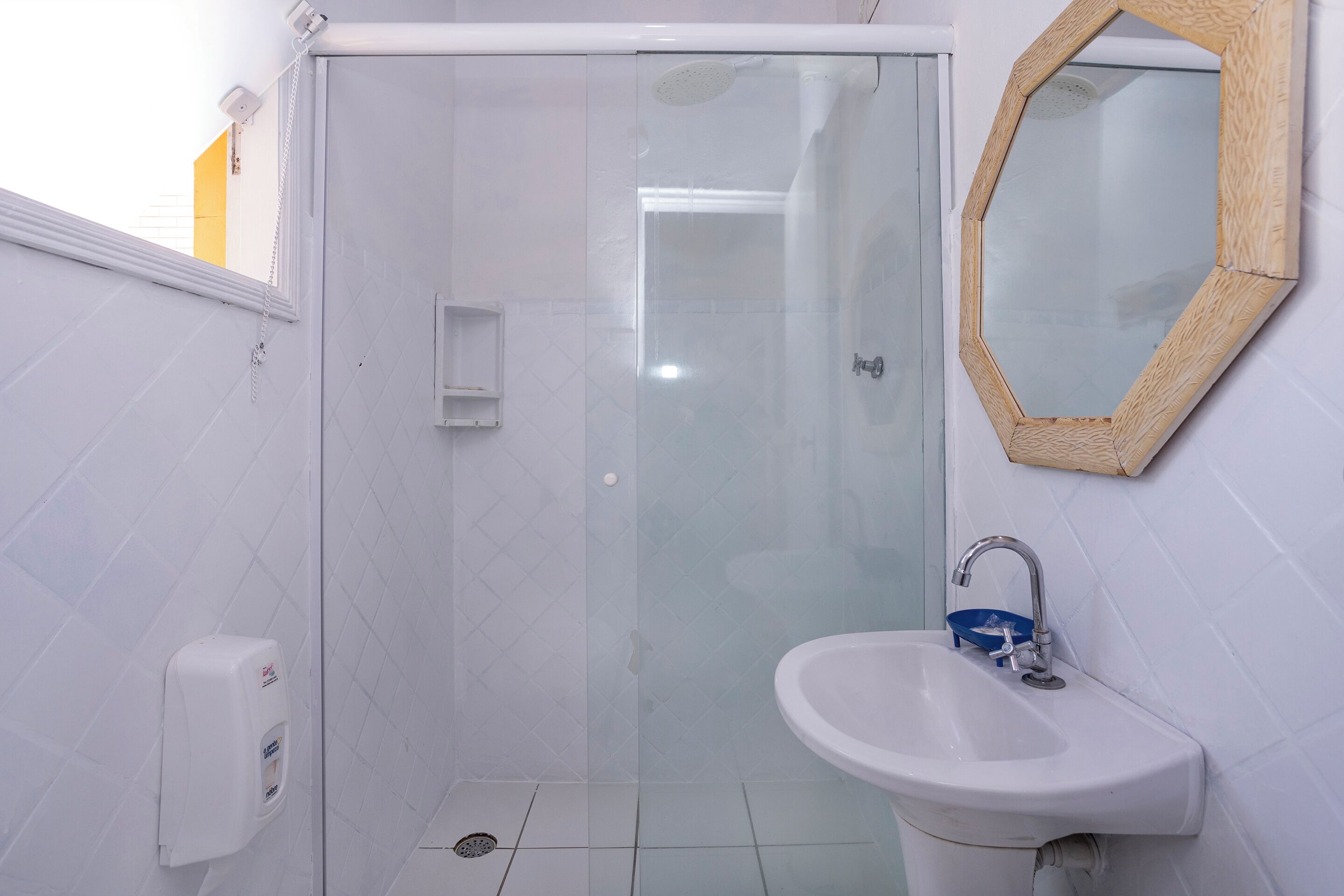 A bathroom with a glass shower enclosure, a sink with a blue soap dispenser, and a wooden-framed mirror.