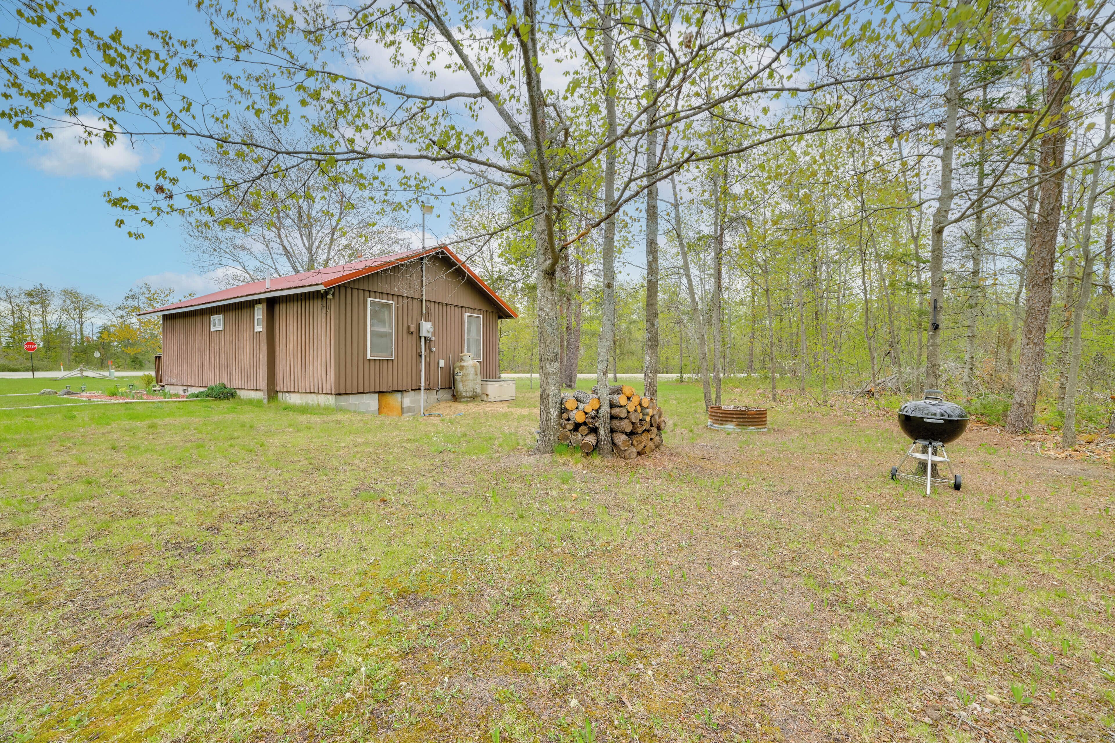 A rustic cabin with a red roof, surrounded by a grassy field and trees.