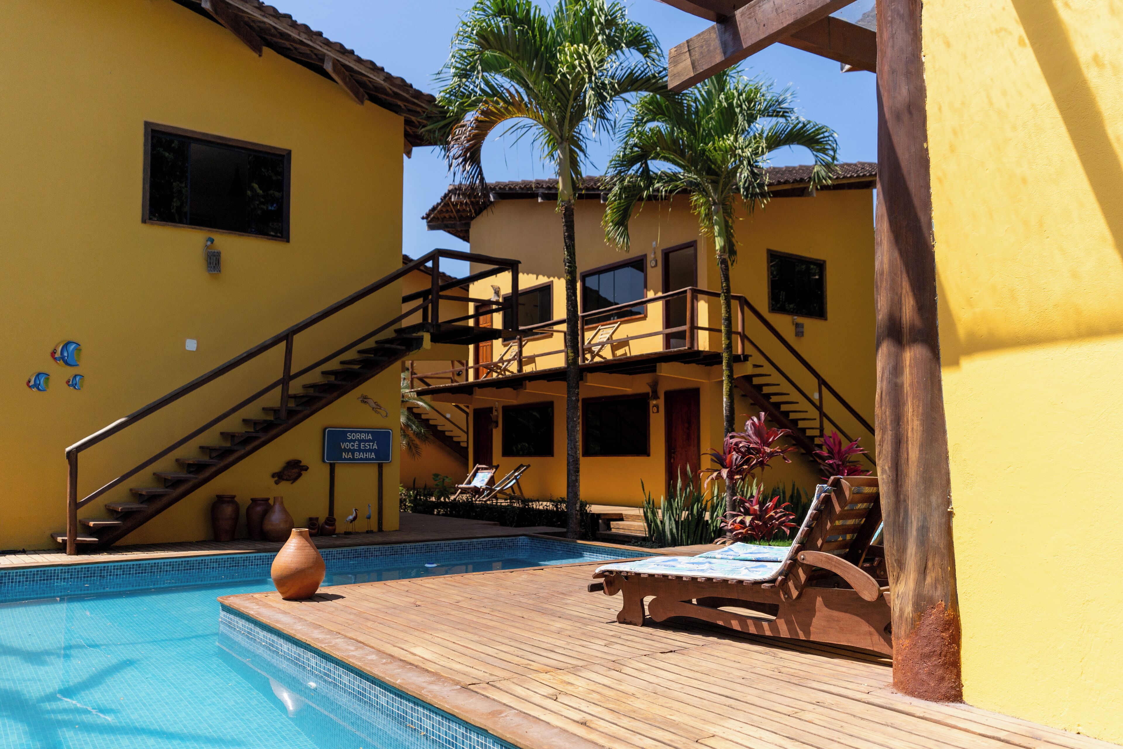A pool area with wooden deck, lounge chairs, and a staircase leading to an upper level.