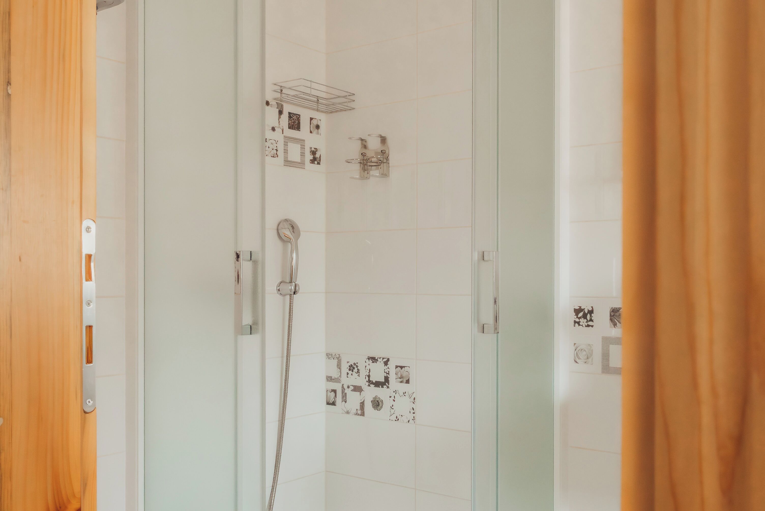 A glass-enclosed shower with a handheld showerhead, a wall-mounted towel rack, and a shower control panel.