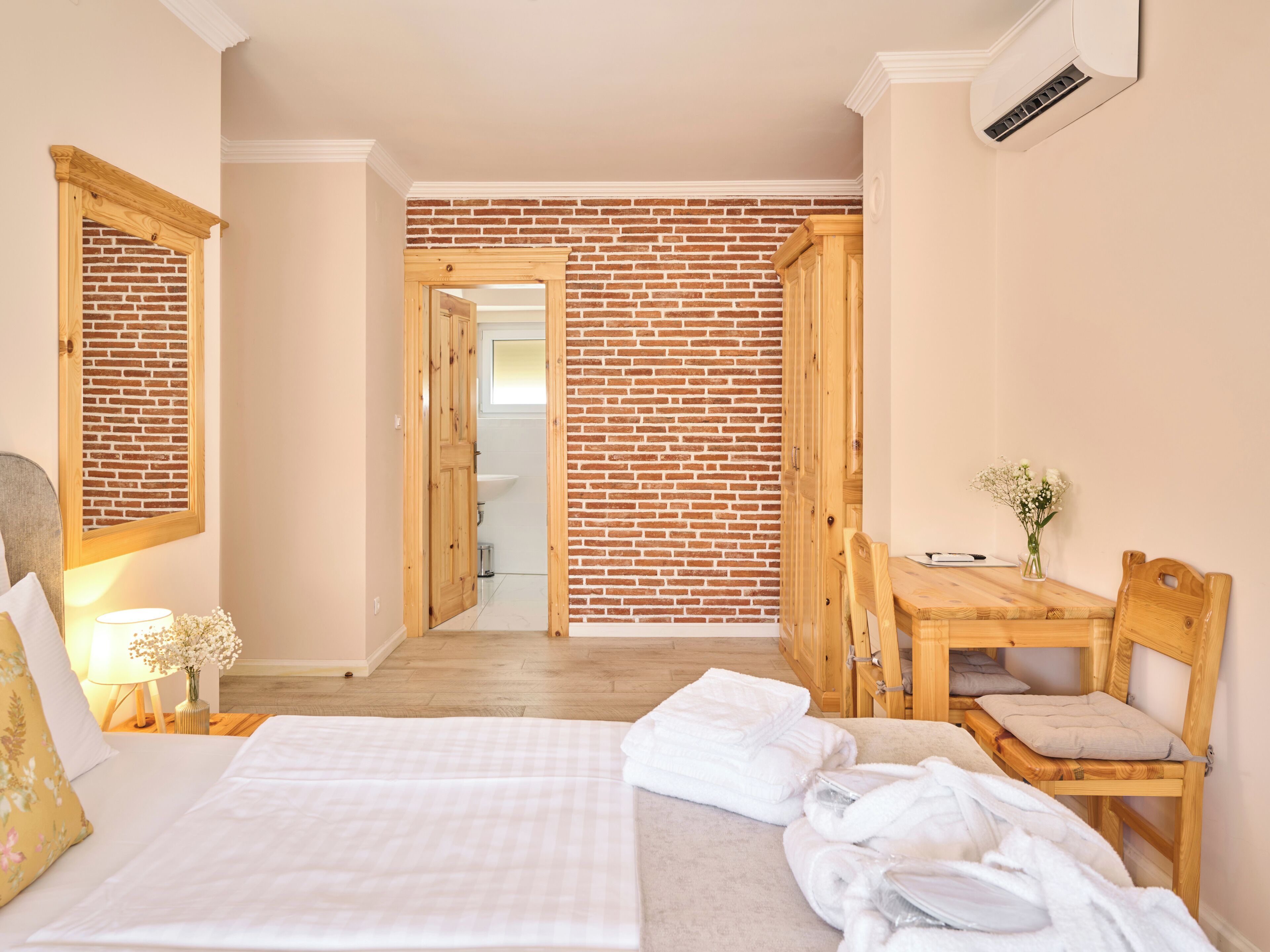 Een slaapkamer met een bed, een houten bureau, een stoel, een raam met uitzicht en een bakstenen muur.