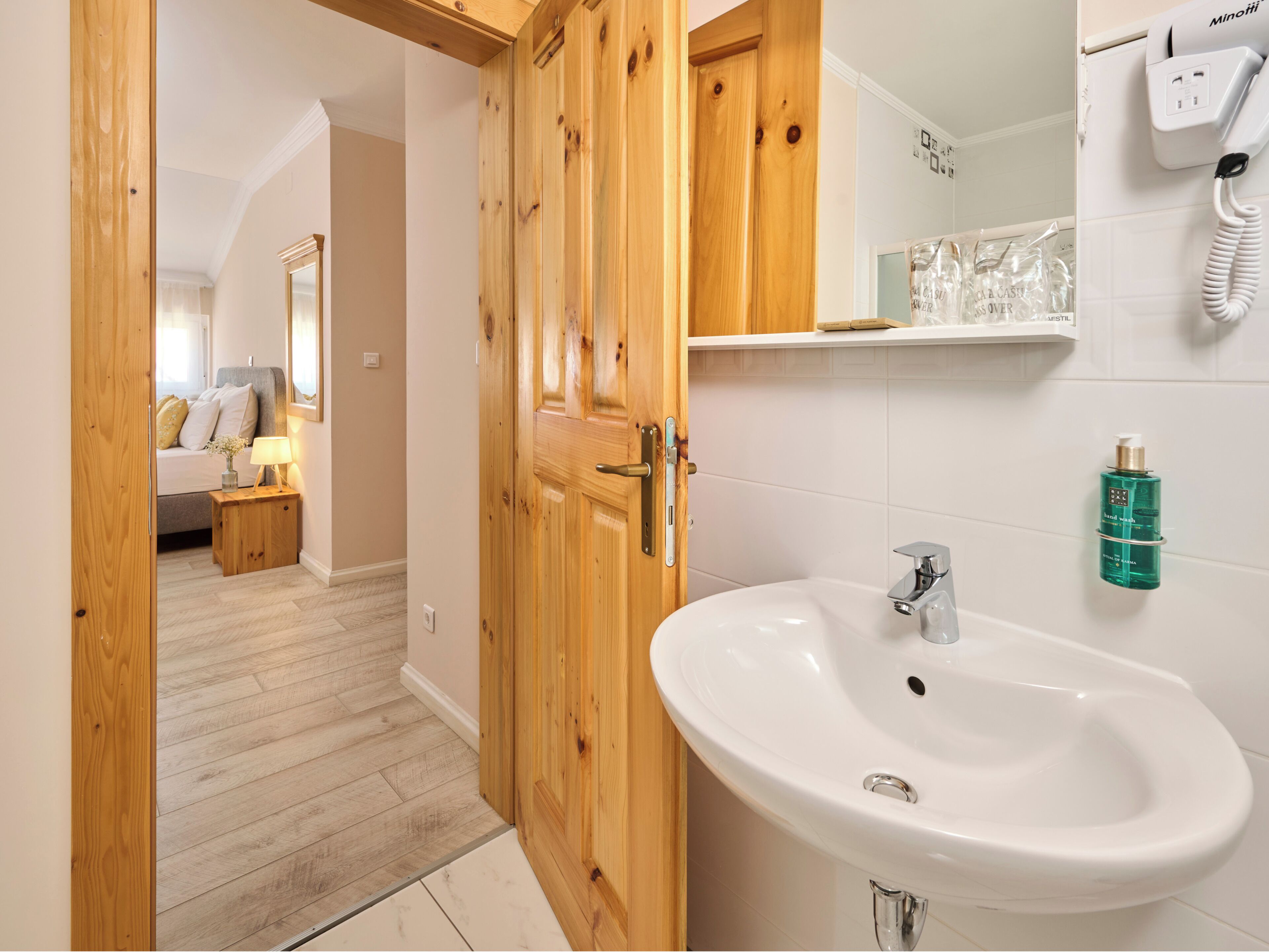 Un baño con puerta de madera, lavamanos blanco y dispensador de jabón.