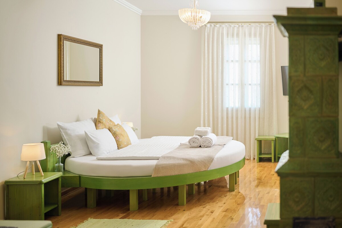 A bedroom with a green bed frame, white bedding, a bedside lamp, a mirror, and a window with curtains.