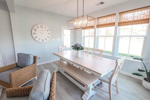 Een eetgedeelte met een houten tafel, banken, rieten stoelen en een grote wandklok.