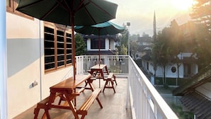 A balcony with wooden tables and benches, a green umbrella, and a view of the surrounding neighborhood. - SF Homey Puri Indah (Cipanas)