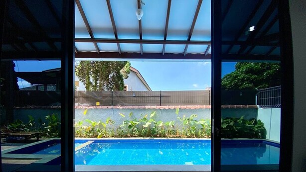 A view of a swimming pool with a wooden deck and a covered area with a metal roof. - SF Homey Puri Indah (Cipanas)