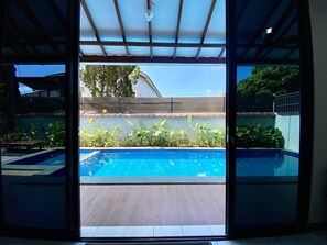 A view of a swimming pool with a wooden deck and a covered area with a metal roof. - SF Homey Puri Indah (Cipanas)