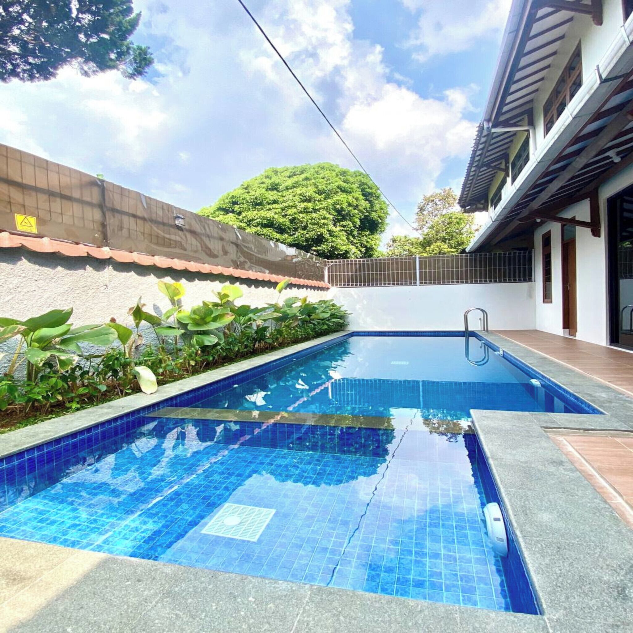 A swimming pool with blue tiles, surrounded by a low brick wall and plants.