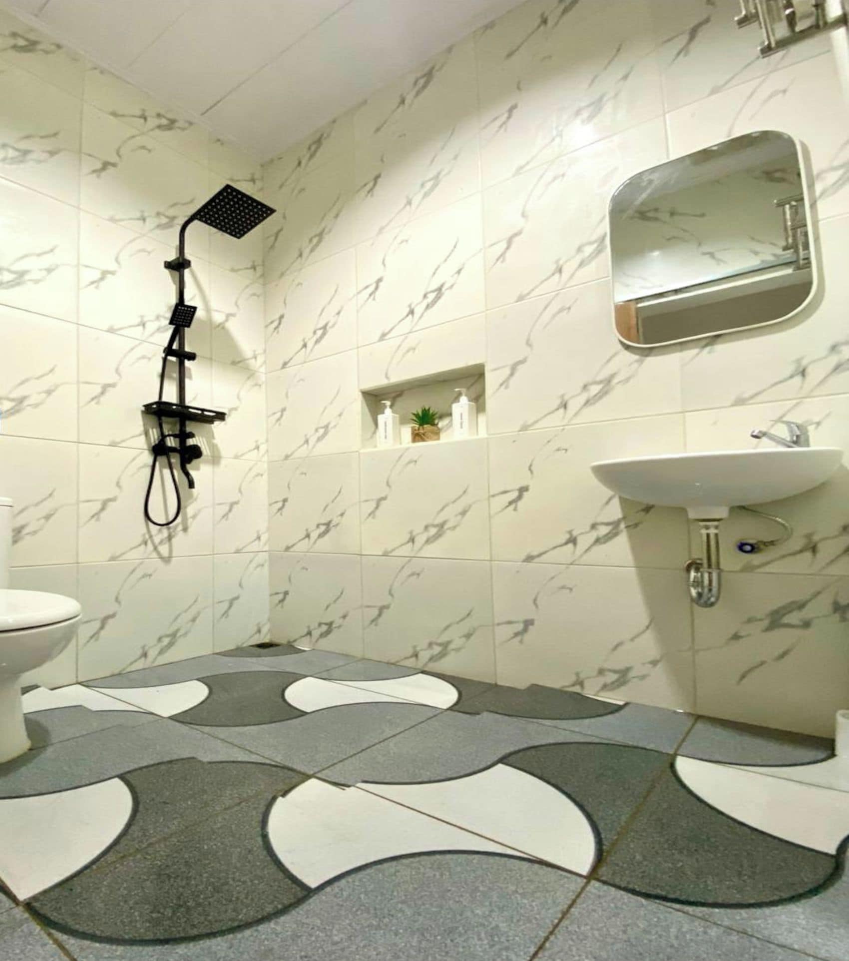 A bathroom with a toilet, a shower, a sink, and a mirror.