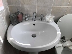 Ein Badezimmer mit einem weißen Waschbecken, zwei Wasserhähnen und einer Toilette.