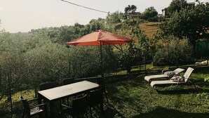Een terras buiten met een tafel, stoelen, een rode parasol en twee loungestoelen.