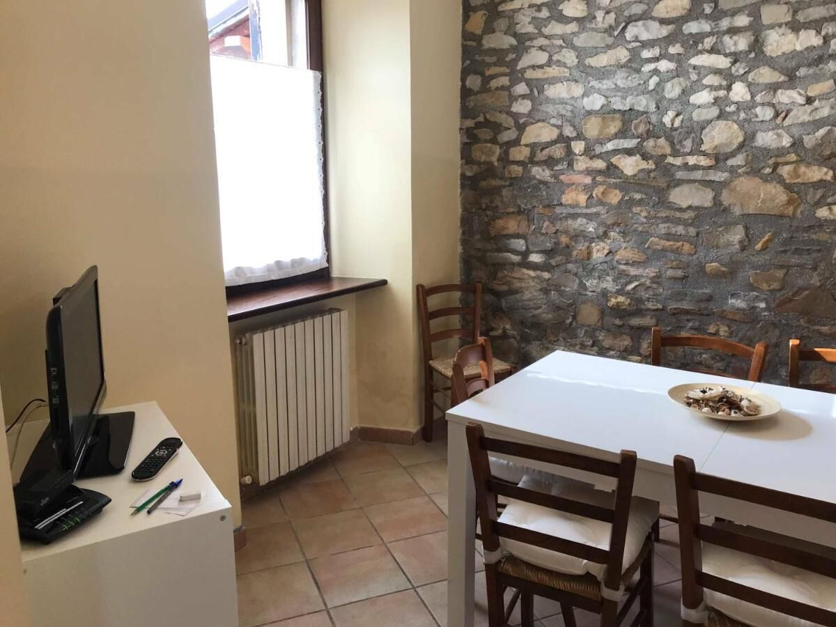 Un coin repas avec un mur en pierre, une table blanche et des chaises. Un ordinateur portable et une télécommande sont posés sur une petite table.