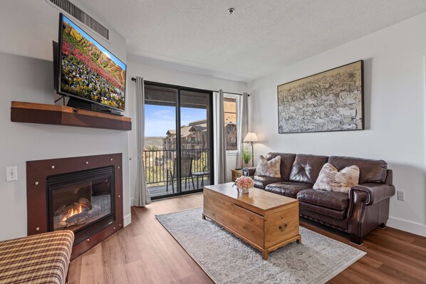 Una sala de estar con chimenea, televisor, sofá y un ventanal grande.