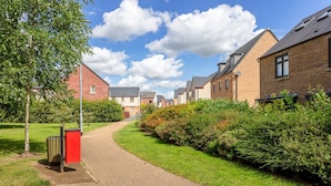 A pathway leading to a row of brick houses with a grassy area and a tree on the left.