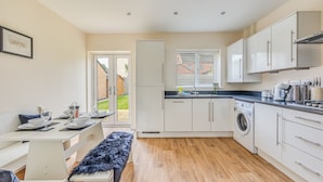 A modern kitchen with white cabinets, a built-in washing machine, and a dining area with a bench and table set for two.