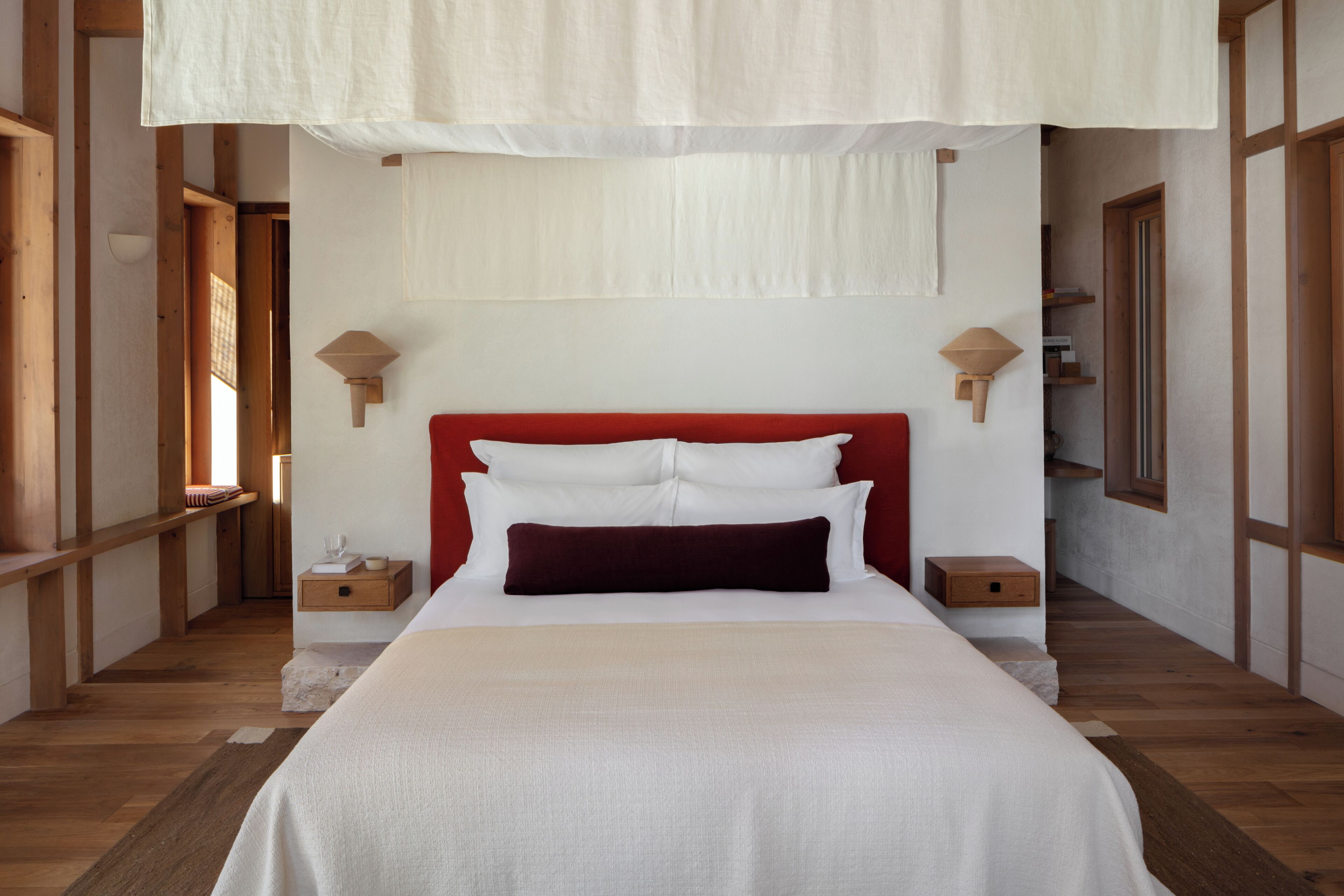 Una cama bien hecha con ropa de cama blanca y roja, cabecero de madera y mesitas de noche con lámparas.