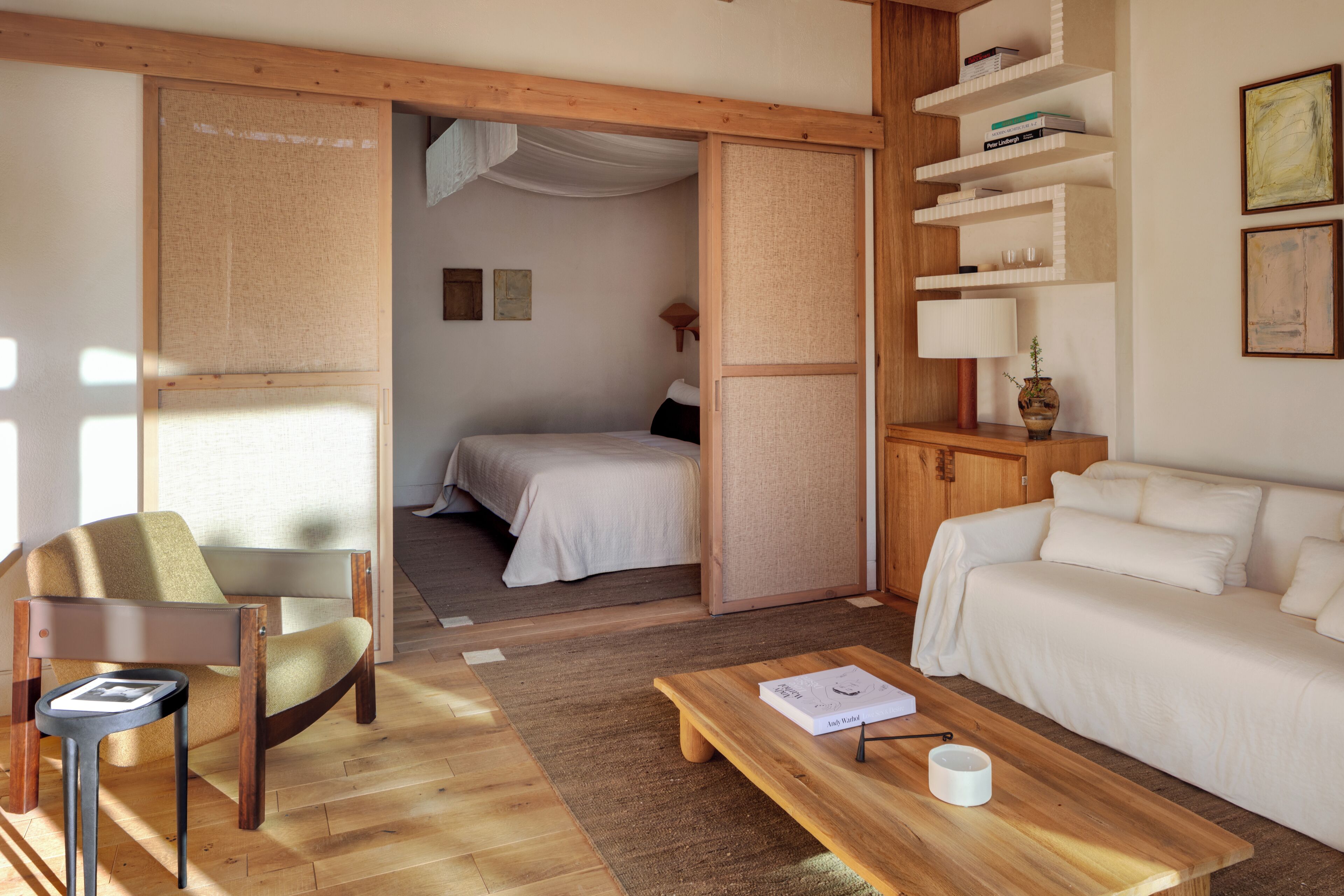 Una habitación con una cama, un sofá, una mesa de centro de madera, una silla y una estantería.