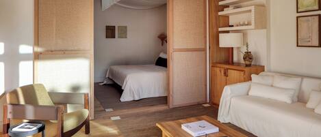 A room with a bed, a sofa, a wooden coffee table, a chair, and a bookshelf.