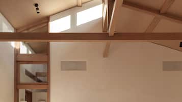 A bedroom with a large bed, wooden beams, a green headboard, and a view of a hallway.