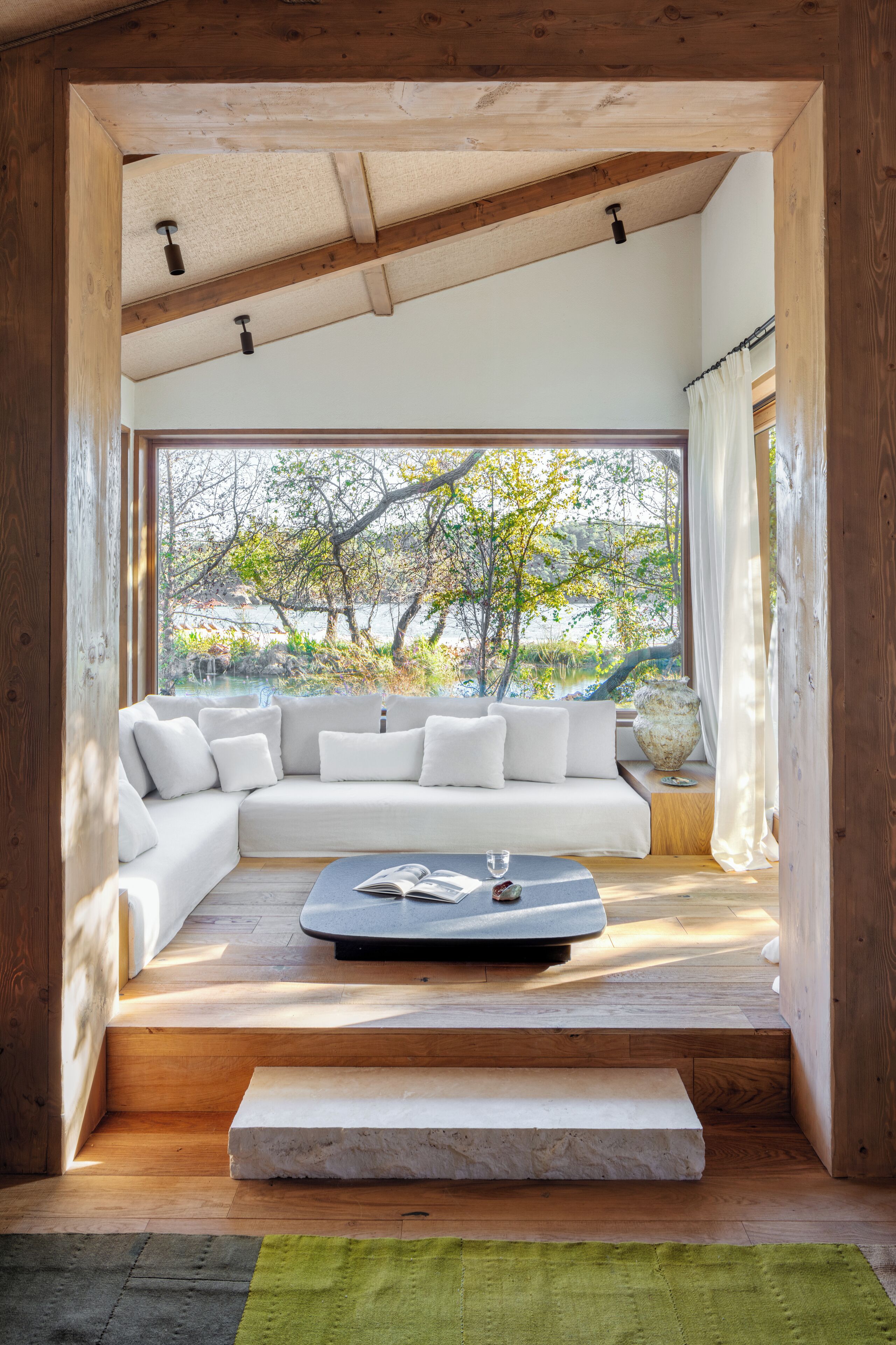 Una sala de estar moderna con un sofá seccional blanco, una mesa de centro y vistas a árboles y agua.