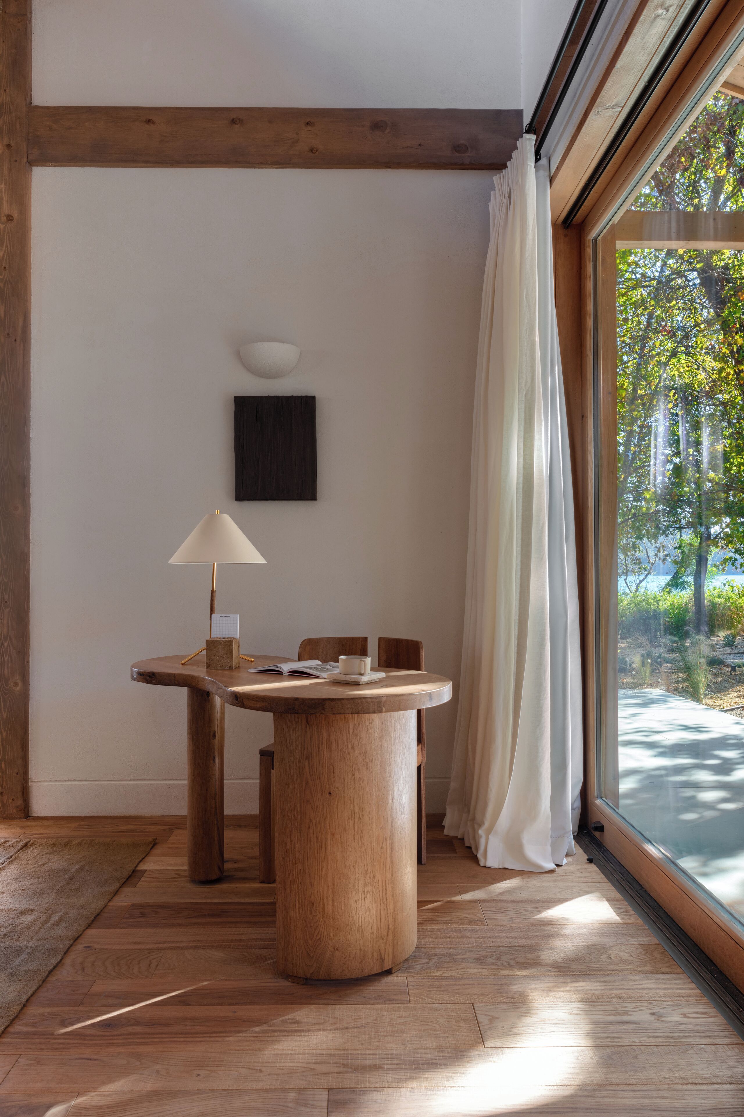 Una mesa de madera para comer con una lámpara, una silla y una mesita con una taza y un libro.