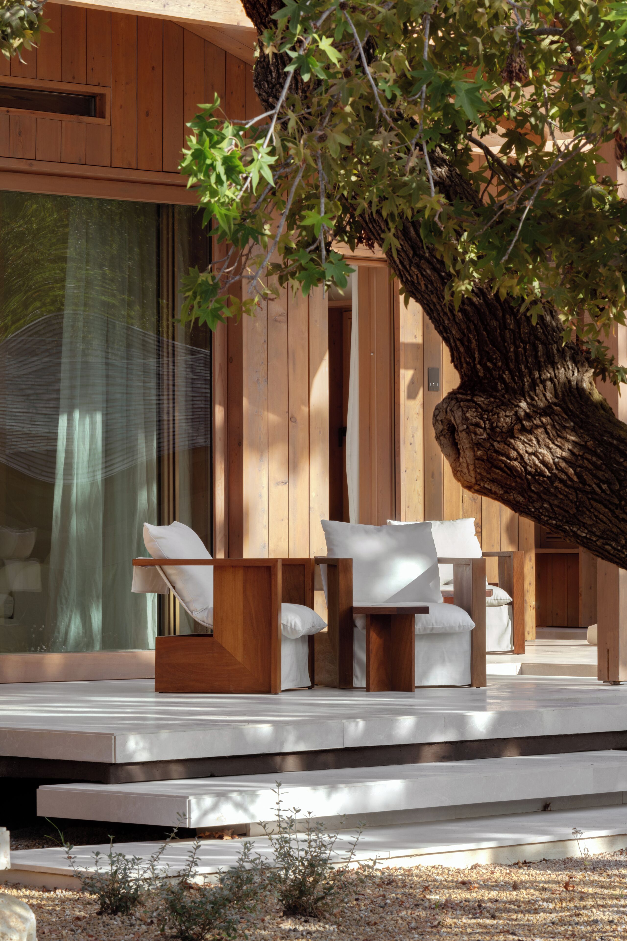 A modern outdoor seating area with wooden furniture and a large tree providing shade.