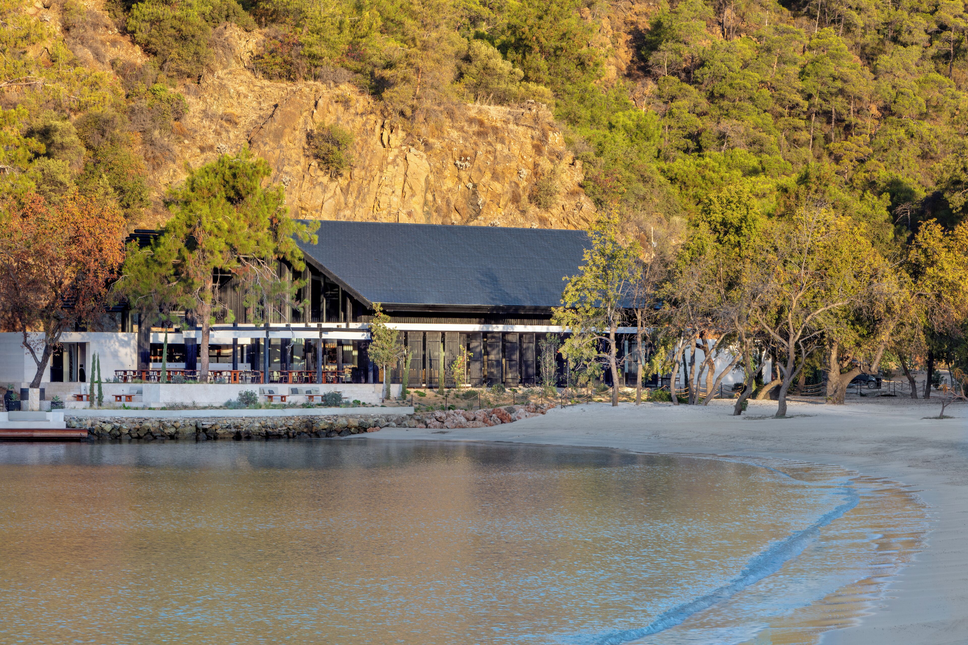 Un bâtiment situé au bord du lac, doté d’un toit plat et entouré d’arbres et d’une plage de sable.