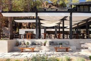 An outdoor seating area with multiple tables and chairs, a stone-paved floor, and a pergola with white canopies. - Ahama - Relais & Châteaux (Fethiye)