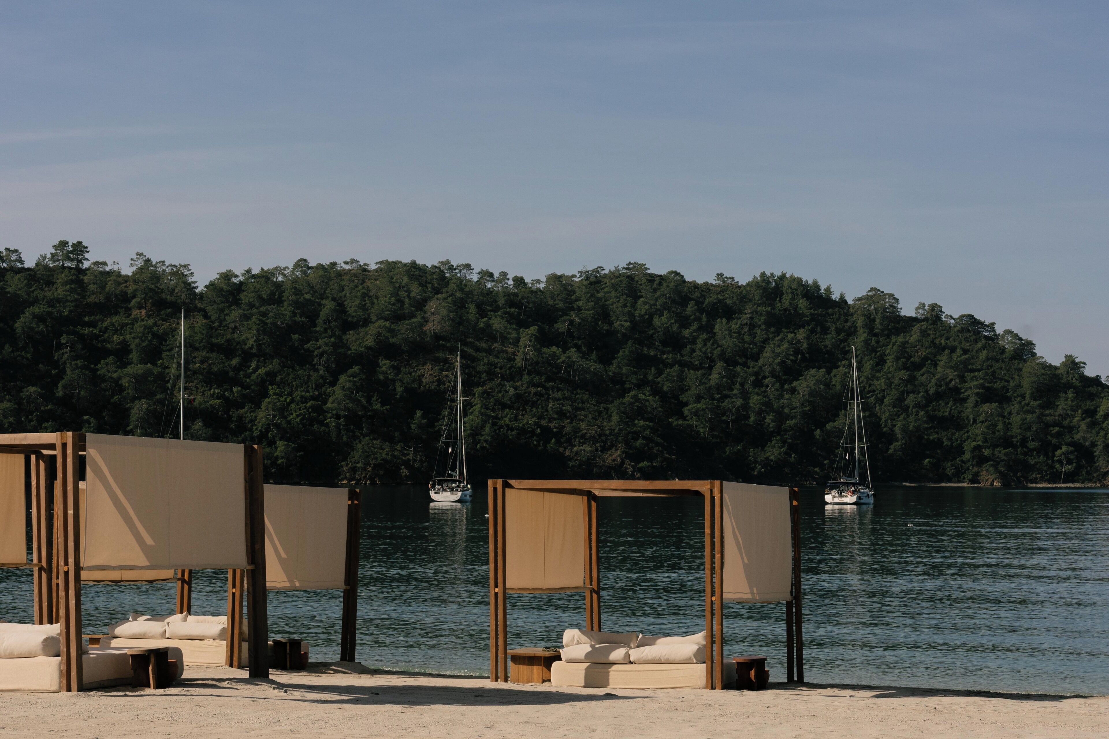 Une plage avec deux cabanes en bois, chacune équipée d’un canapé et d’une table.
