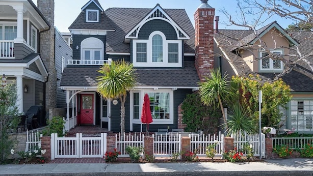 A two-story house with a red front door, white picket fence, and a brick chimney.