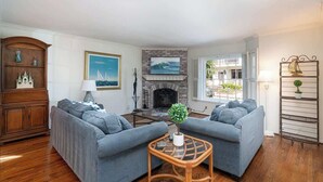 A living room with two grey sofas, a fireplace, a wooden cabinet, and a view of the outside balcony.