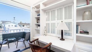 A balcony with a white desk, a chair, and a lamp. There are bookshelves with books and a decorative jar.