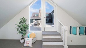 A cozy attic bedroom with a view of the backyard, a potted plant, and a decorative pillow.