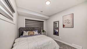 A bedroom with a bed, a window with blinds, a bedside table, a mirror, and a motivational poster on the wall.