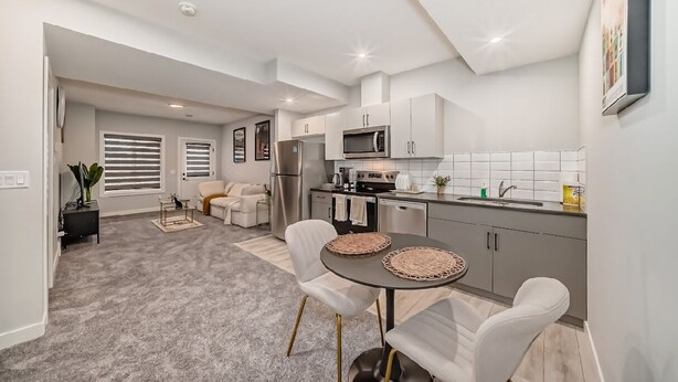 A modern kitchen with white cabinetry, a microwave, and a sink. There is a dining area with a round table and chairs.