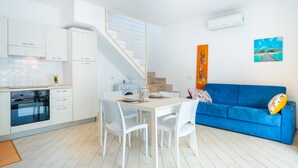 Ett modernt kök med vita skåp, ett matbord med stolar, en blå soffa och en trappa.