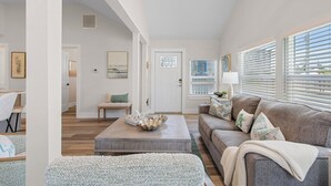 A spacious living room with a large window, a ceiling fan, and a wooden coffee table. - Coconut Sunsets A & B on Estero Blvd, 7 Bedroom Hom by RedAwning (Fort Myers Beach)