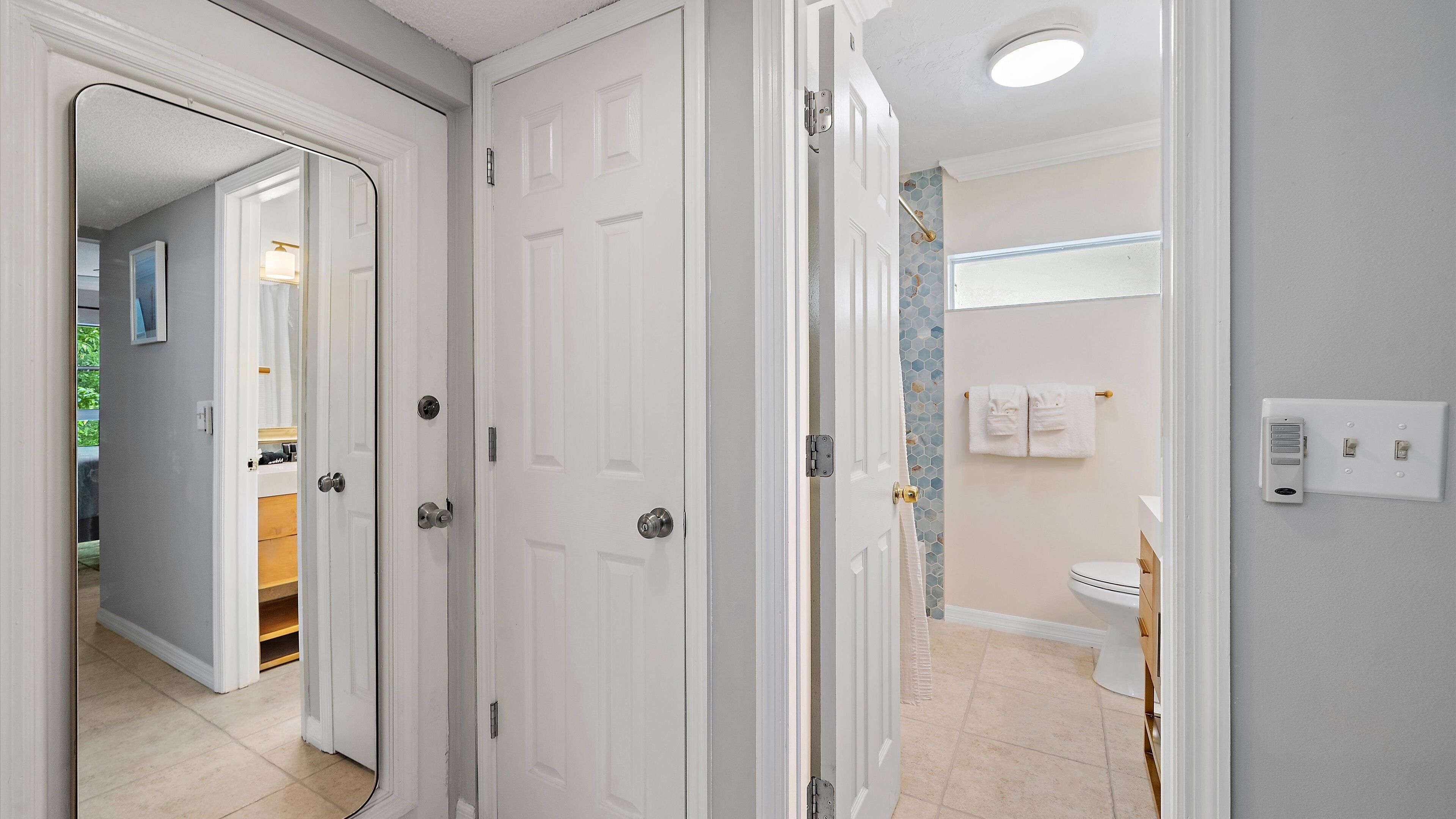 A hallway with white doors leading to a bathroom with a toilet and a shower.
