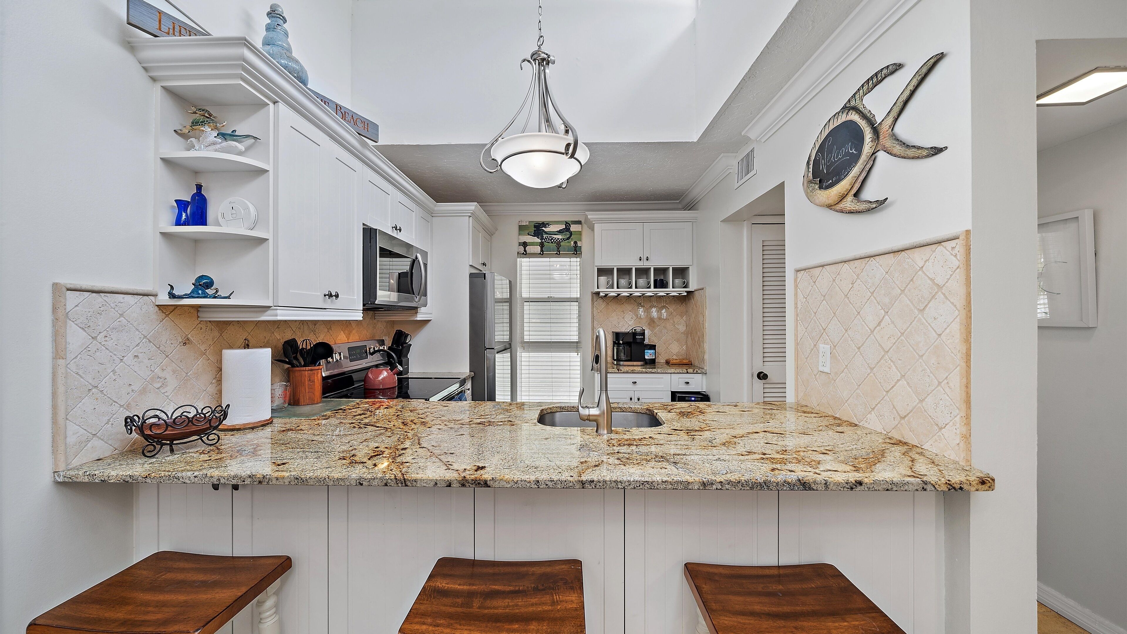 A kitchen with a granite countertop, white cabinetry, and a hanging light fixture.