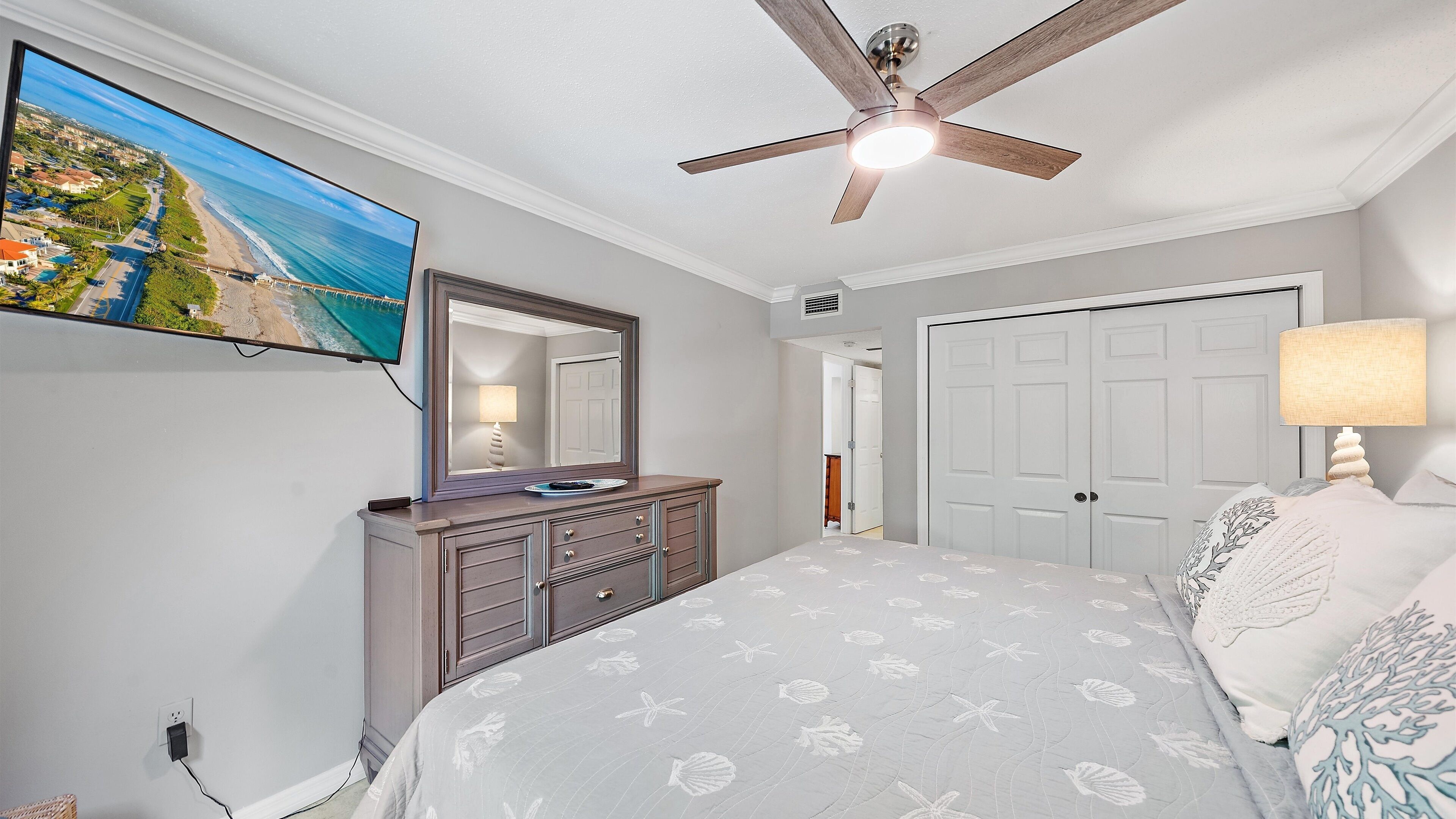 Quarto com cama, cômoda, ventilador de teto, televisão e porta.