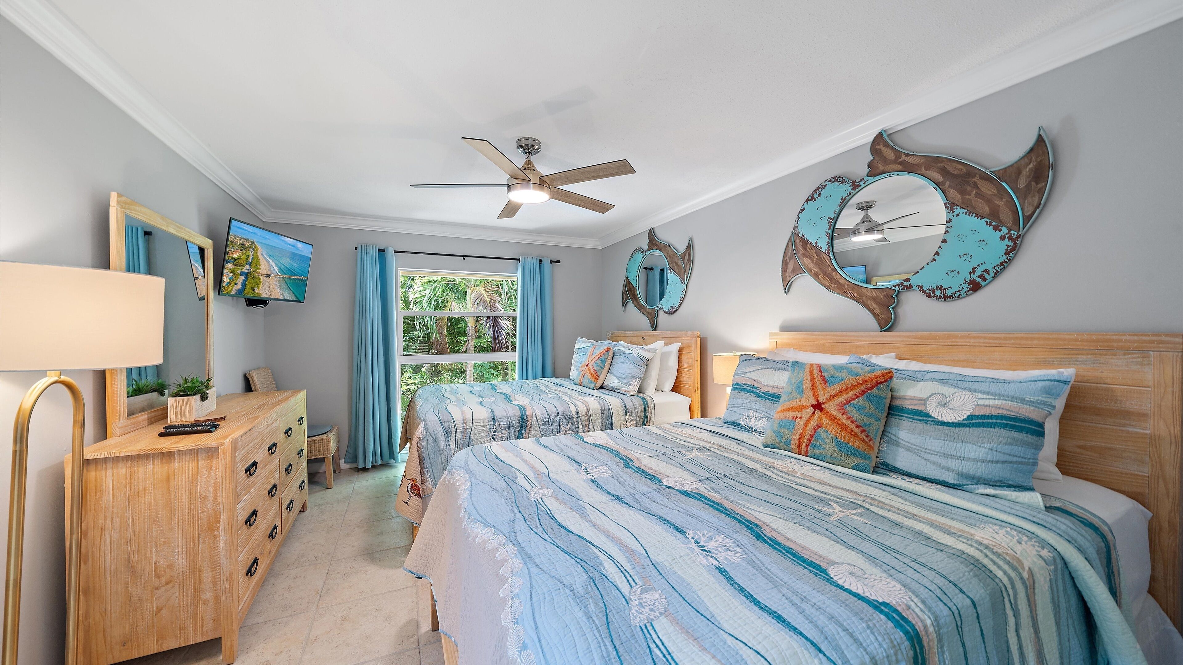 Un dormitorio con cama, cómoda, ventilador de techo, un espejo grande y una ventana con cortinas.