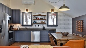 Une cuisine moderne avec des meubles gris, un réfrigérateur en acier inoxydable, un lave-vaisselle et une table à manger en bois, assortie de chaises orange.