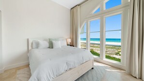 Ein Schlafzimmer mit einem großen Bett, Meerblick und einem fensterbepflanzten Fenster.