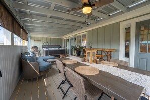 Egy fedett, szabadtéri étkezőhely, ahol egy hosszú asztal, fonott bútorok és egy mennyezeti ventilátor található.