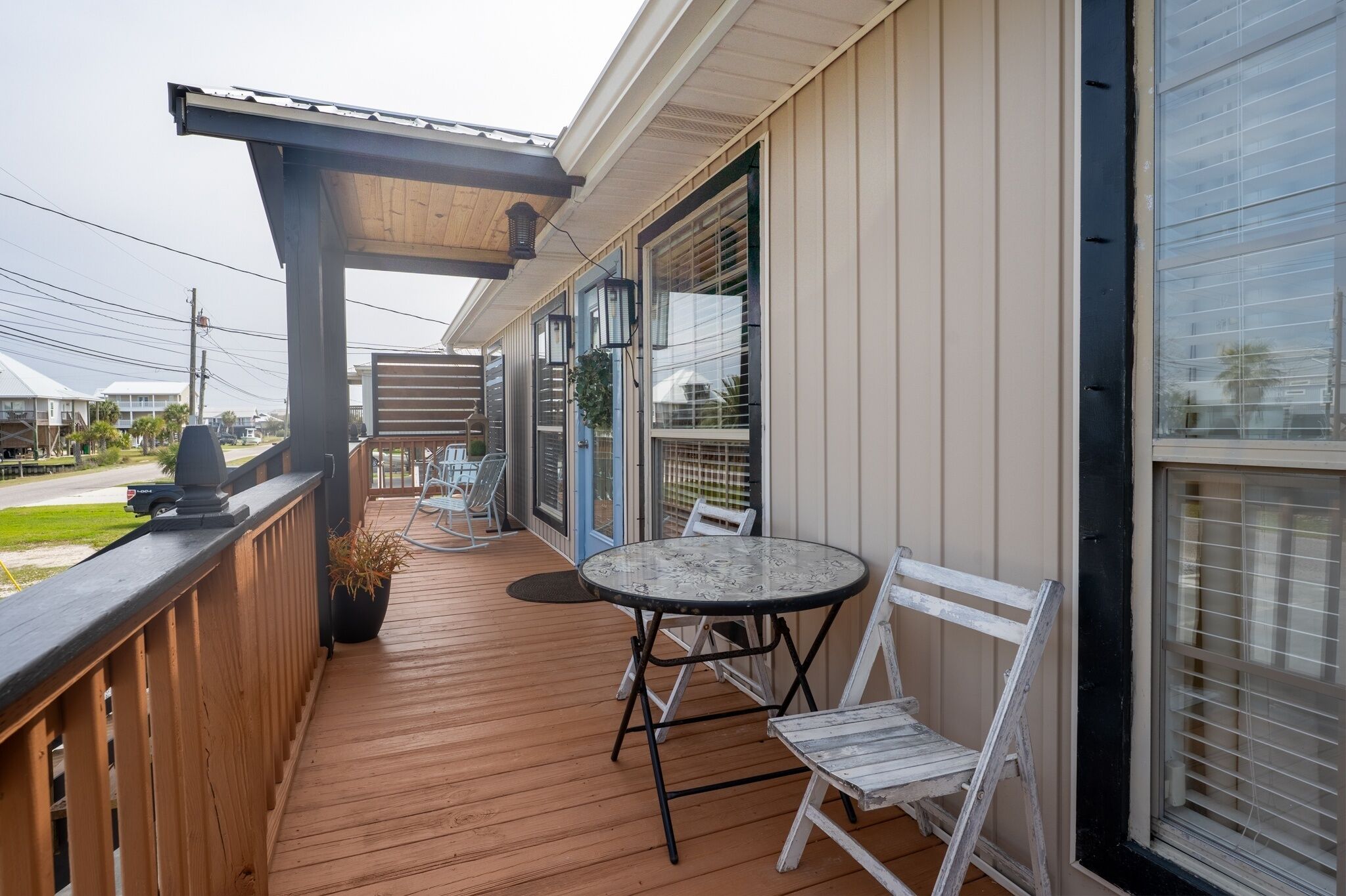 A covered outdoor area with a wooden deck, a round table with chairs, and a pergola with a lantern.