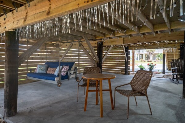 A covered outdoor seating area with a swing, wicker chairs, and a round table.