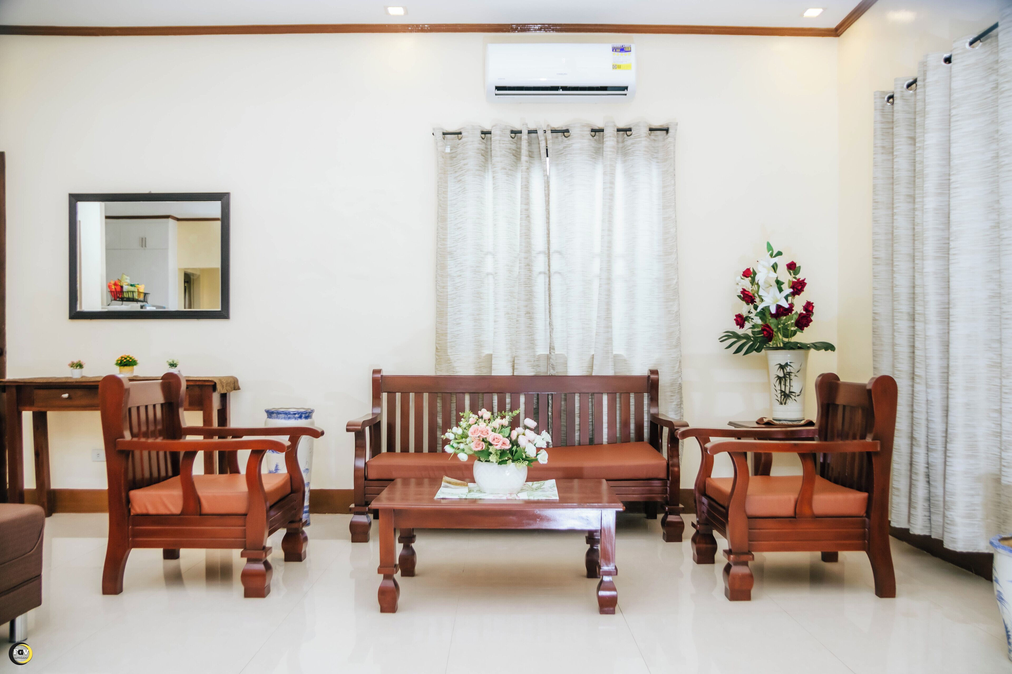 A living room with a sofa, two chairs, a coffee table, a mirror, and a potted plant.