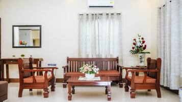 A living room with a sofa, two chairs, a coffee table, a mirror, and a potted plant.