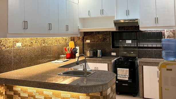 Una cocina moderna con armarios blancos, encimera de granito y estufa integrada.