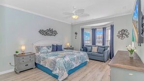 Ein Schlafzimmer mit Bett, Nachttischen, Kommode, Deckenventilator und einem Fenster mit Vorhängen.